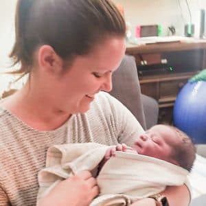 A new mother smiling as she holds her swaddled newborn